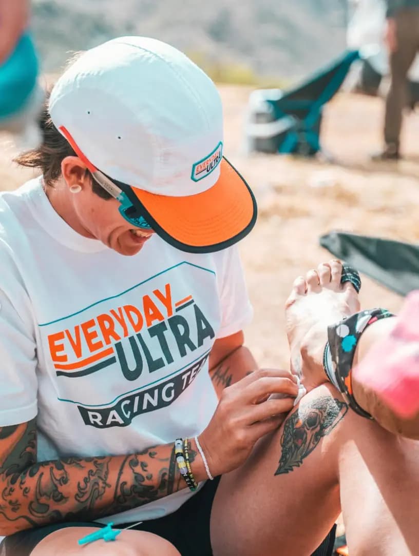 A crew member tends a runner's leg at a desert aid station