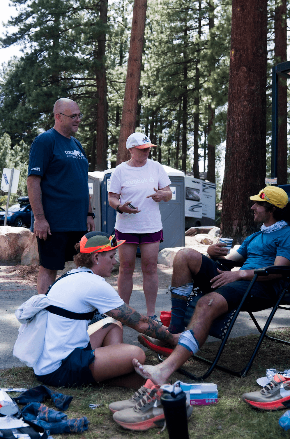 Crew work on a seated runner's legs at a forest aid station